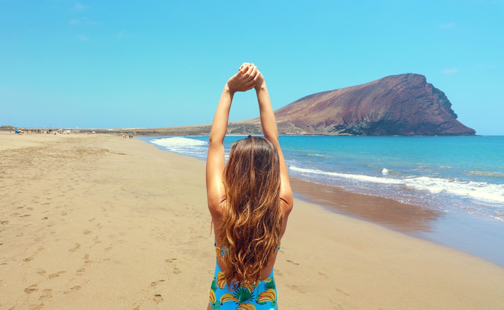 Back view beautiful woman doing stretching exercises on the beach in Playa La Tejita, Tenerife