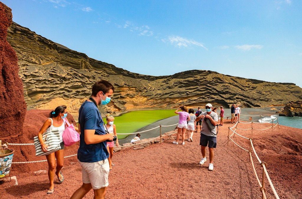 El Golfo, Lanzarote/Spain - July 27, 2020: Tourists at Lago Verde (or Charco de Los Clicos) viewpoint are wearing surgical face masks and adhere to social distancing during coronavirus crisis in Spain
