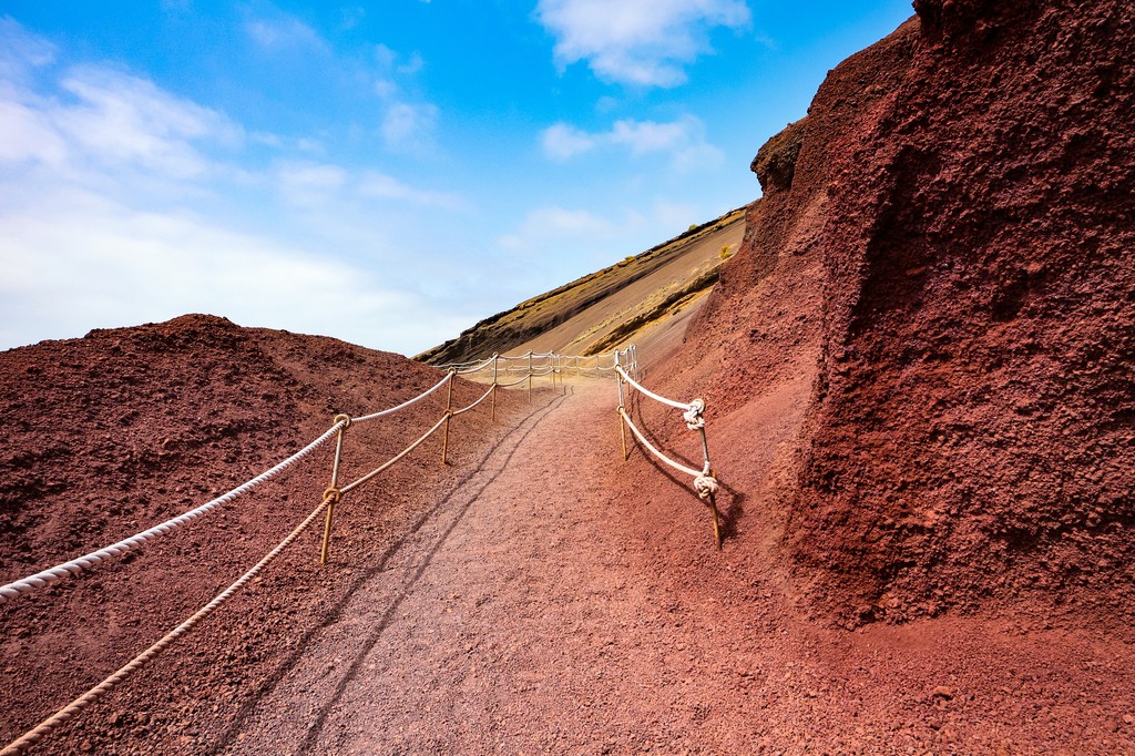 Lonely footpath through a stunning red volcanic rock landscape under a blue sky, seen in El Golfo, Lanzarote, Canary Islands, Spain. 