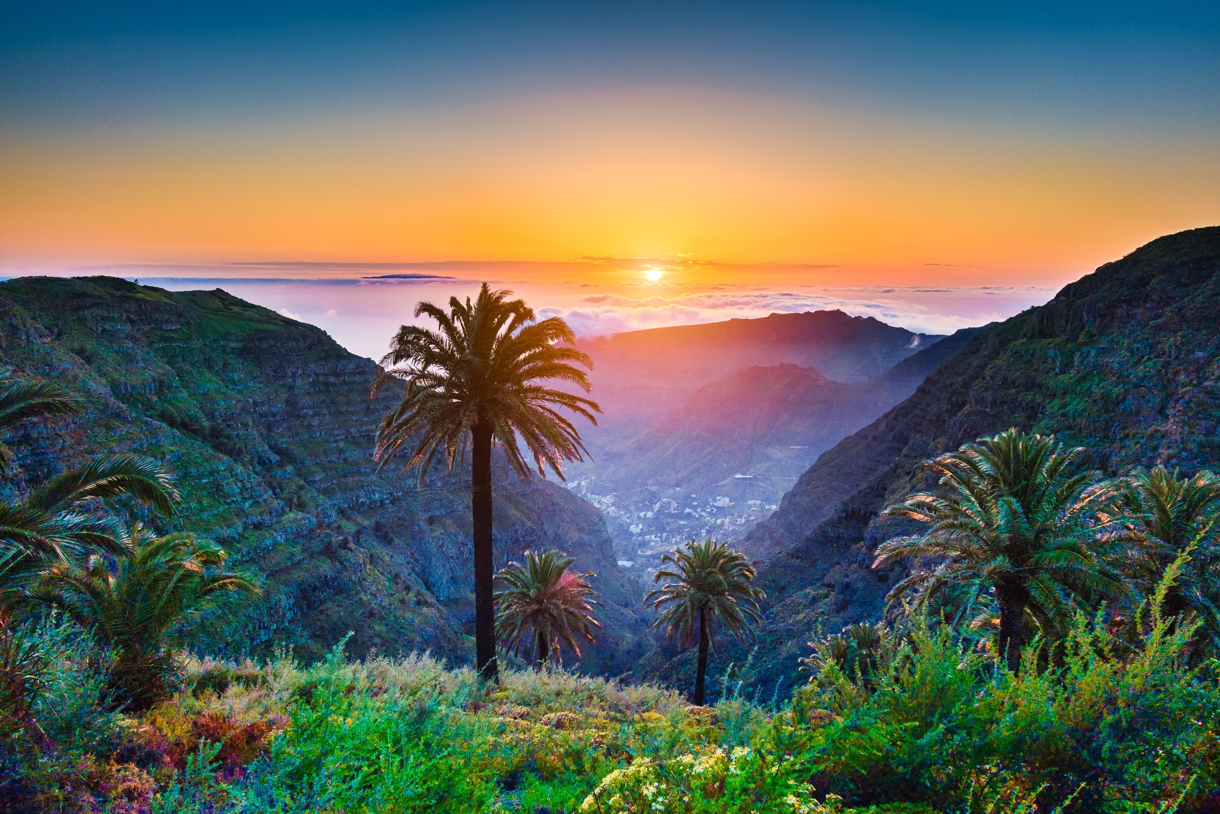 Piękny widok z niesamowitej tropikalnej scenerii z egzotycznymi palmami i górskimi dolinami nad szerokim otwartym morzem w złotym świetle wieczorem o zachodzie słońca z błękitnym niebem i chmurami w lecie, Wyspy Kanaryjskie, Hiszpania