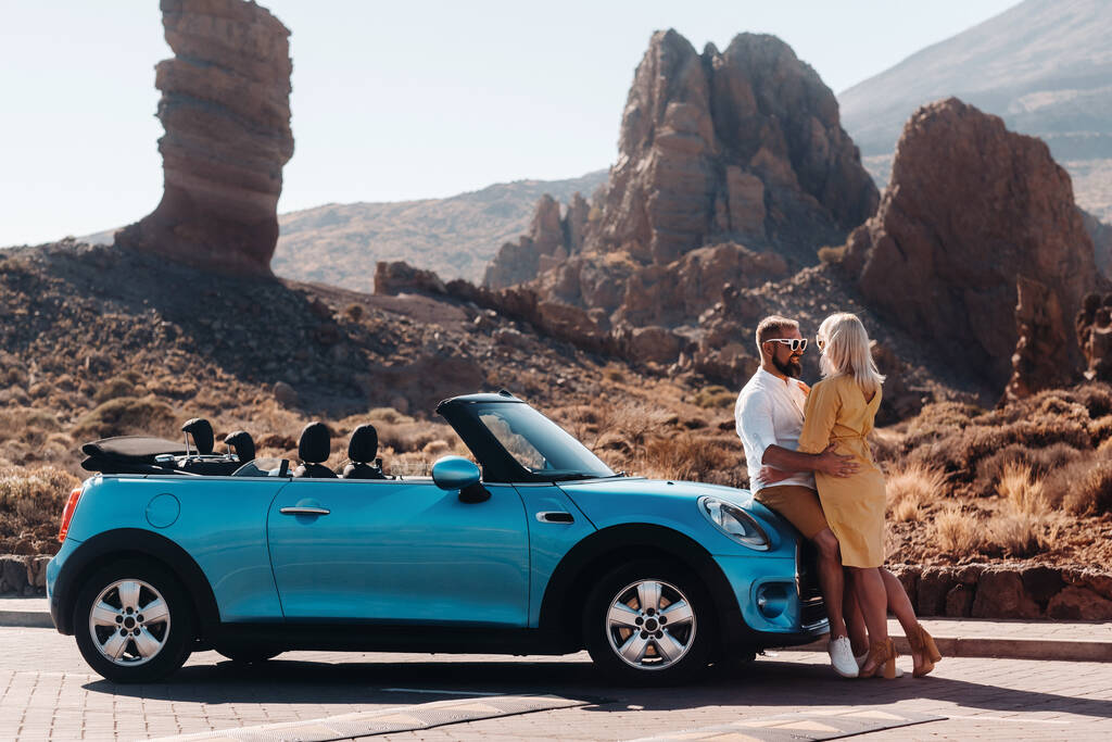 a woman and a man wearing glasses in a convertible car on a trip to the island of Tenerife. The crater of the Teide volcano, Canary Islands,Spain