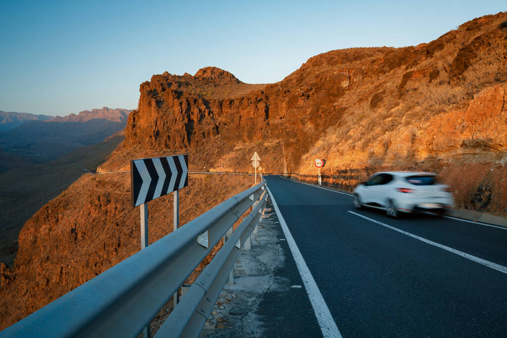 Cars are driving on road between peaks of Gran Canaria mountains in sunset light.