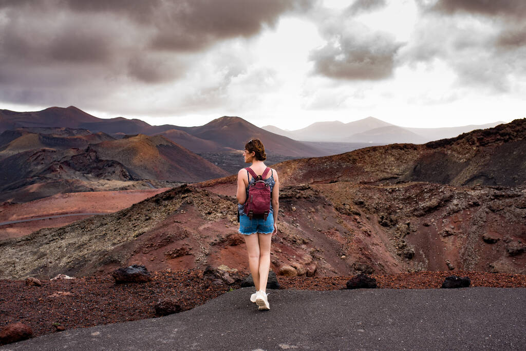 Young woman with a backpack contemplating the volcanic area Timanfaya Natural Park, in Lanzarote, in Lanzarote