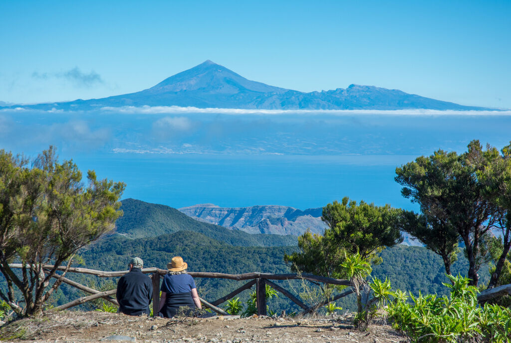 Couple looking from Alto de Garajonay, Garajonay national park, La Gomera on Teide volcanic mountain, with clear view on the south coast of Tenerife island and atlantic ocean - shot with zoom lens