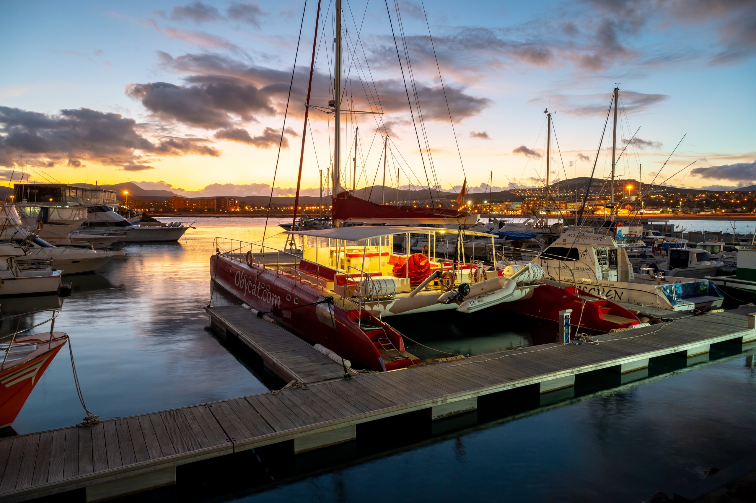 Fuerteventura, Hiszpania, 28 lutego 2023 r., Jachty i motorówki w zatoce oceanicznej Fuerteventura o zmierzchu po zachodzie słońca, hotele na wzgórzu w oddali, licencja: shutterstock/By CinemaPhoto