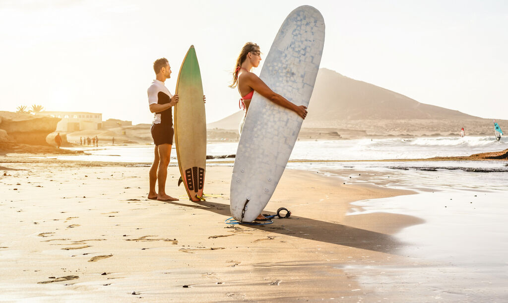 Para surferów czeka na wysokie fale na plaży - sportowcy z deskami surfingowymi o zachodzie słońca., licencja: shutterstock/By DisobeyArt