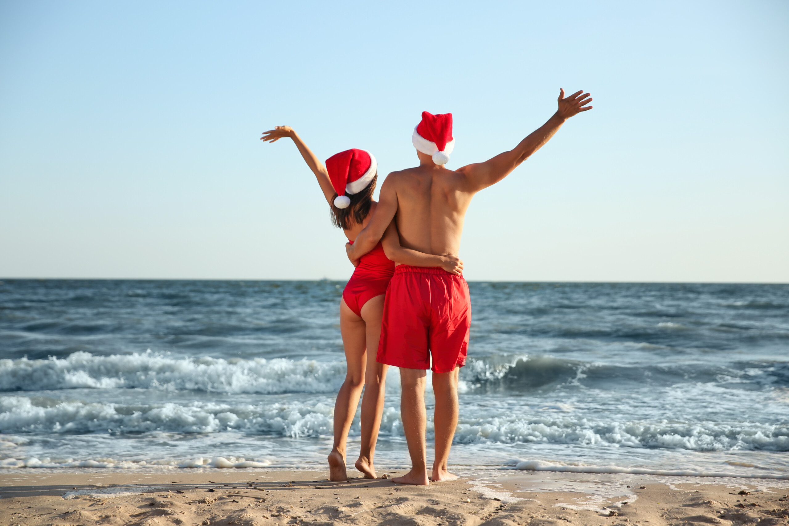 Para uchwycona w czapkach Mikołaja na plaży podczas ferii świątecznych.